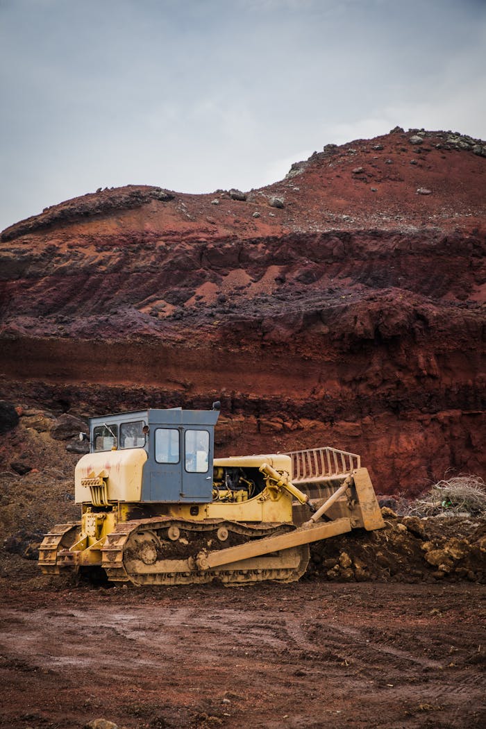 services-01 A yellow bulldozer excavating in a rugged red earth quarry under a cloudy sky.